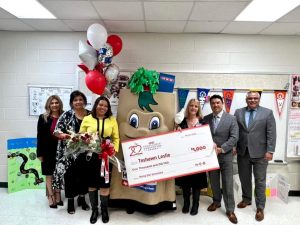 Teshawn Leslie receives an oversized $1,000 check for an HEB Excellence in Education Award, alongside the H E Buddy mascot and colleagues.